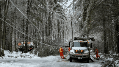 A Hydro car on a road with broken trees and a worker trying to fix the issue during the April 2025 Ice storm in Ontario 