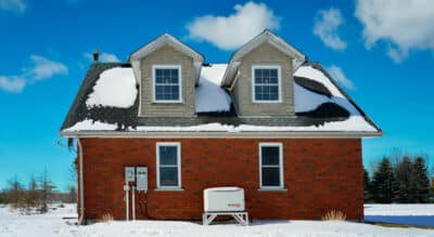a house with snow on the roof and Generac standby backup home generator installed with a transfer switch in Shanty Bay Ontario by Platinum number one Generac dealer in Ontario